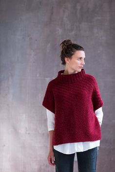 a woman standing in front of a wall wearing a red knitted sweater and jeans