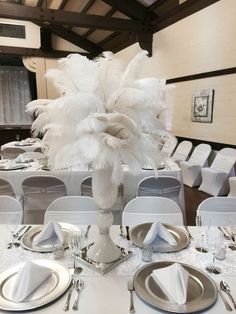 the table is set with silverware, plates and white centerpieces on it