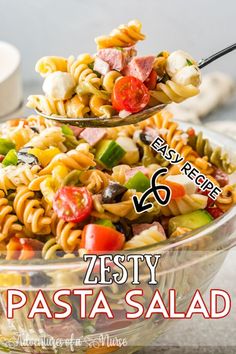 pasta salad in a glass bowl being lifted with a serving spoon over it and the words zesty pasta salad below