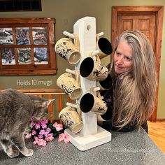 a woman with long hair standing next to a cat looking at cups on a stand