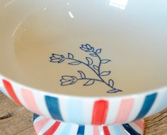 a white bowl with blue and red flowers on it sitting on a wooden table top