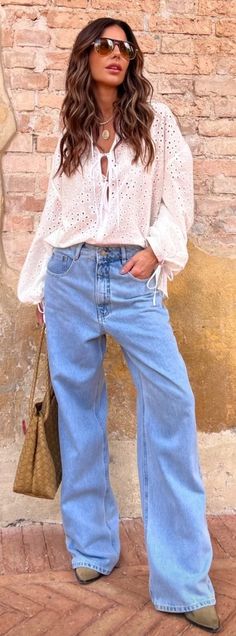 a woman standing in front of a brick wall with her hands on her hips and wearing wide jeans