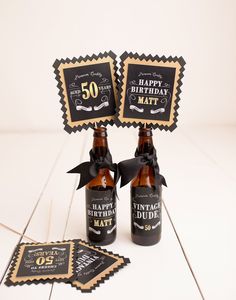 two beer bottles with happy birthday tags on them sitting next to some coasters that say 50th