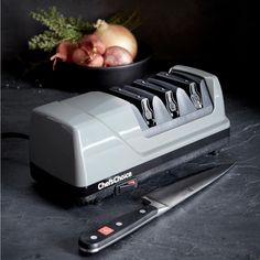 a knife and some onions in a bowl next to a knife sharpener on a table