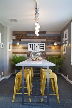 a dining room table with yellow stools in front of it and a clock on the wall