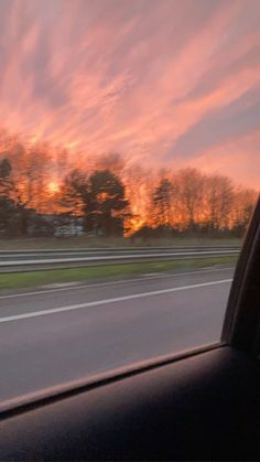 the sun is setting behind some trees on the side of the road as seen from inside a car