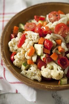 a bowl filled with cauliflower, tomatoes and cucumbers