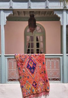 an orange and pink rug hanging on the side of a building in front of a window