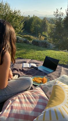 a woman sitting on a bed with a laptop and food in front of her,