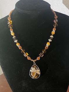 This 19-inch beaded necklace is made with varying hues of brown glass beads with silver-colored accents.  The 1.5-inch pendant is a tiger's eye teardrop with a silver-colored dragon fly. Brown Necklace With Silver Beads For Gift, Beaded Teardrop Brown Necklace, Brown Beaded Teardrop Necklace, Brown Crystal Necklace With Faceted Beads For Gift, Brown Beaded Necklace, Dragon Fly, Tiger's Eye, Beaded Necklaces, Tiger Eye