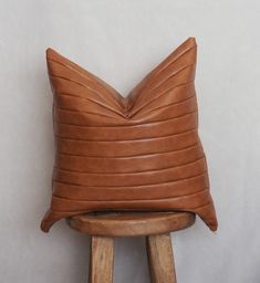 a brown leather pillow sitting on top of a wooden stool next to a white wall