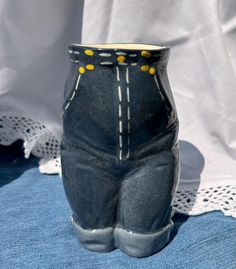 a blue vase with yellow buttons on the bottom and jeans on the inside, sitting on a white doily