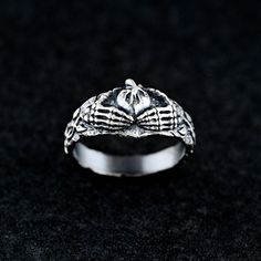 This sterling silver ring combines the gothic allure of skeleton hands with the timeless symbolism of the Claddagh ring, representing love, loyalty, and friendship. The intricate design features two skeleton hands holding a heart, crowned by a subtle flame motif, making it an ideal piece for those who embrace dark, edgy aesthetics with deep meaning. Details:     Material: 925 Sterling Silver     Finish: Oxidized highlighting its refined and timeless appeal. Our pieces are crafted with love and m Vintage Metal Rings For Halloween, Gothic Skull Ring For Halloween, Gothic Skull Open Ring Gift, Skull Shaped Ring As Halloween Gift, Symbolic Skull Rings For Halloween, Halloween Skull Rings Symbolic Style, Gothic Metal Skull Ring, Silver Symbolic Skull Ring For Halloween, Symbolic Silver Skull Ring For Halloween