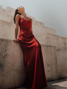 a woman in a long red dress leaning against a wall with her head resting on the ledge