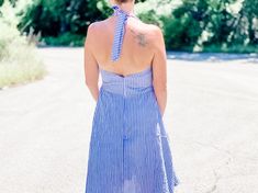 a woman wearing a blue and white striped dress is standing in the middle of an empty road