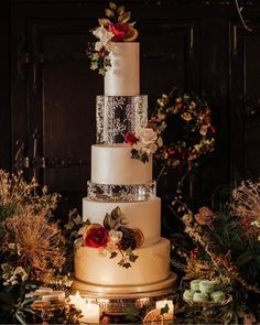 a three tiered wedding cake with red flowers on top and greenery around it