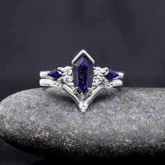 a blue and white diamond ring sitting on top of a gray rock with three diamonds