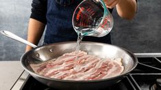 a person pouring water into a pan filled with meat