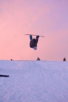 a man flying through the air while riding a snowboard on top of a snow covered slope