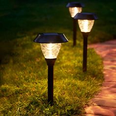 three solar powered lights on the grass in front of a brick path at night time