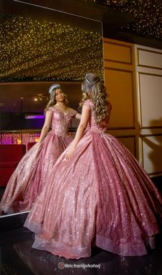 two women dressed in pink gowns standing next to each other on a black surface