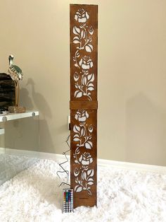 a tall wooden sculpture with flowers on it's sides and a remote control next to it