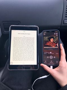 a person holding an electronic device next to a book in their lap and headphones