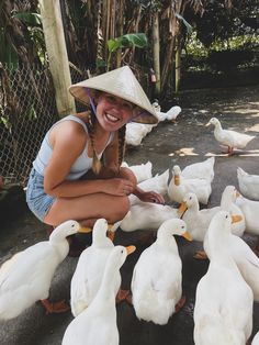 a woman kneeling down next to ducks with a hat on her head and smiling at the camera