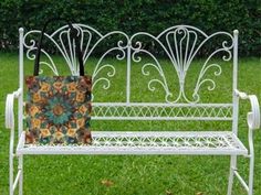 a white wrought iron bench with an umbrella on it's back in the grass