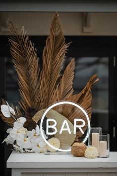 a bar sign sitting on top of a white table next to flowers and candle holders