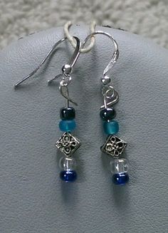 These earrings are made with silver flower spacer beads, blue seed beads, and black metallic seed beads. Silver-plated earring hooks and wire were used. Adjustable Blue Earrings With Black Beads, Blue Beaded Metal Earrings, Blue Metal Beaded Earrings, Blue Dangle Earrings With Black Beads, Blue Metal Beaded Earrings For Pierced Ears, Blue Dangle Jewelry With Black Beads, Adjustable Blue Beaded Earrings With Silver Beads, Blue Silver Beads Drop Earrings, Blue Silver Beaded Drop Earrings