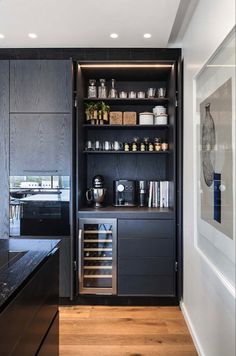 a kitchen with black cabinetry and wooden flooring in the center is lit by recessed lights