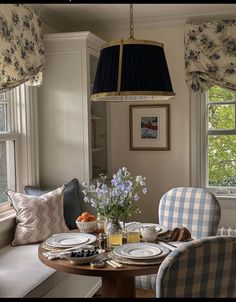 a dining room table set for two with place settings and flowers in the centerpiece