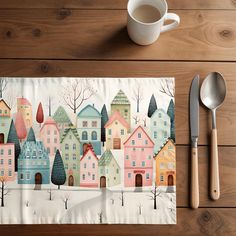 a place mat with houses and trees on it next to a spoon, fork and knife