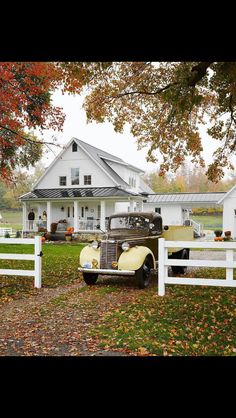 an old car is parked in front of a white house with autumn leaves on the ground