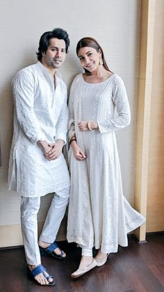 two people standing next to each other in front of a wooden wall and flooring