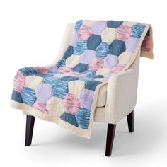 an upholstered chair with a patchwork blanket on it's back and legs