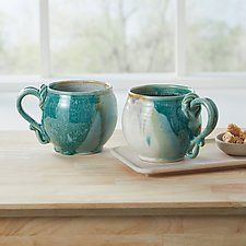 two coffee mugs sitting on top of a wooden table next to a small bowl