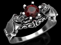 a silver ring with a red stone in the center and two skulls on each side