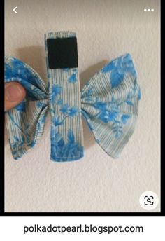 a hand holding a blue and white flowered hair bow on top of a wall