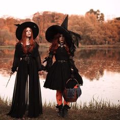 two women dressed in witches costumes standing next to each other near a lake and trees