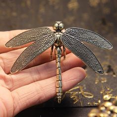 a hand holding a dragonfly figurine on top of a table next to gold numerals