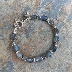 This bracelet is handmade using natural, quality labradorite ovals and disks. Sterling Hill Tribe silver in patterned throughout. Strung on sturdy, high quality beading wire and closes with a sterling Hill Tribe silver flower stamped toggle and flower bud dangle. Please message me if you need a different size or clasp. 7.5 inch bracelet Labradorite ovals: 9 x 7mm approximately Labradorite disks: 4.5mm approximately Your jewelry will arrive in a cotton lined kraft box within a padded postal envel Handmade Jewelry Bracelets Not On The High Street, Sterling Silver Beaded Jewelry, Silver Beaded Jewelry, Wire Wrapped Jewelry Diy, Bracelets Design, Jewelry Making Bracelet, Diy Bracelet Designs, Labradorite Bracelet, Hill Tribe Silver