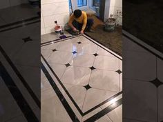 a man kneeling down on the ground working on a tile floor in a room with black and white tiles