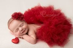 a newborn baby wearing a red tutu and holding a heart