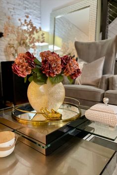 a glass table topped with a vase filled with flowers on top of a metal tray