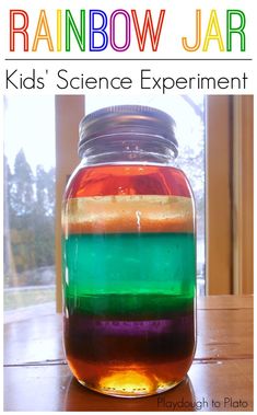 a jar filled with rainbow colored liquid sitting on top of a table next to a window