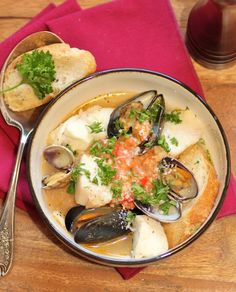 a bowl filled with clams and bread on top of a red napkin next to a spoon