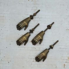 four brass hand handles are shown on a white brick wall, and one is in the shape of an outstretched hand