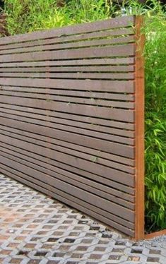 a wooden slatted fence in front of some bushes and plants on the sidewalk